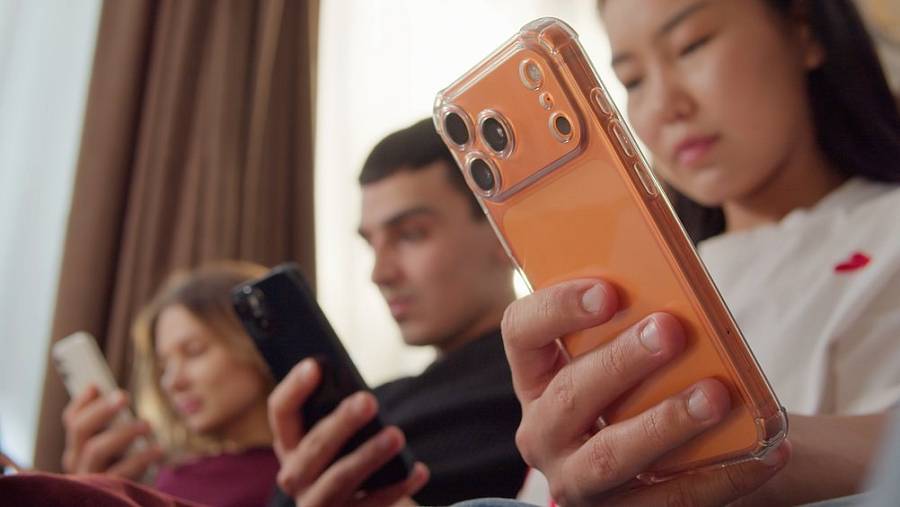 Drei Jugendliche sitzen nebeneinander und schauen konzentriert auf ihre Smartphones.